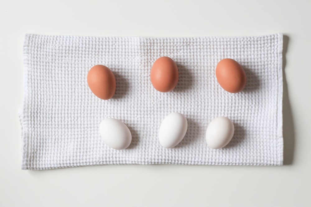 six white and brown eggs on white towel