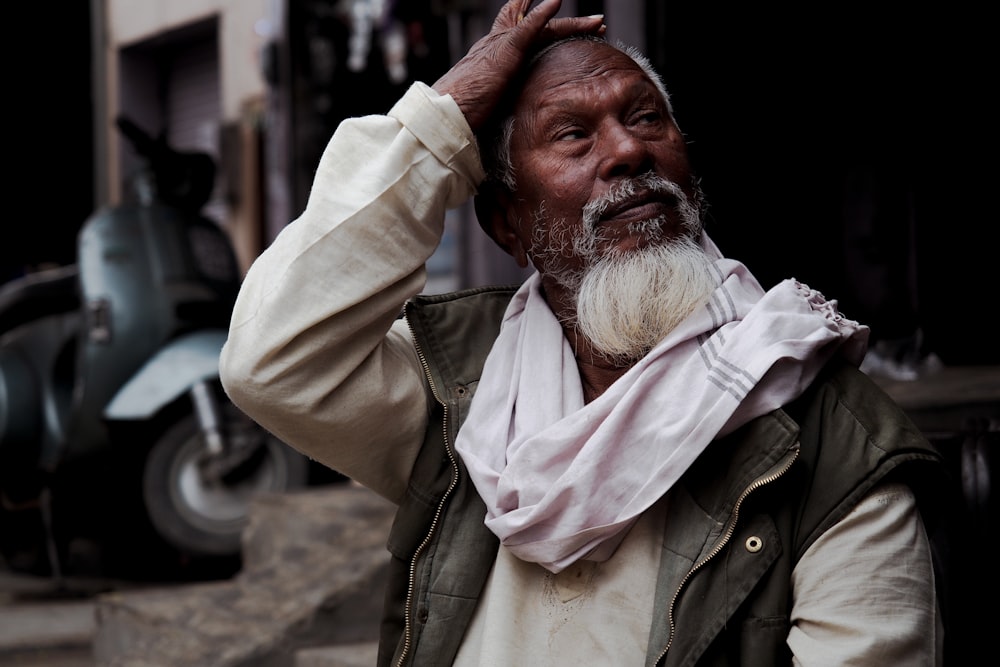 man with white scarf touching his forehead