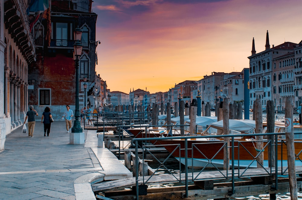 man beside woman walking near boats on body of water along houses