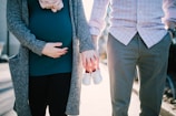 man standing beside pregnant woman holding baby's shoes during daytime