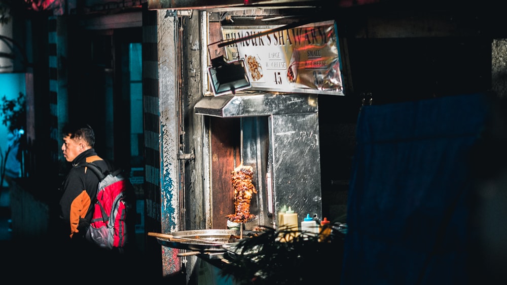 man in black jacket with red backpack standing near gyro machine