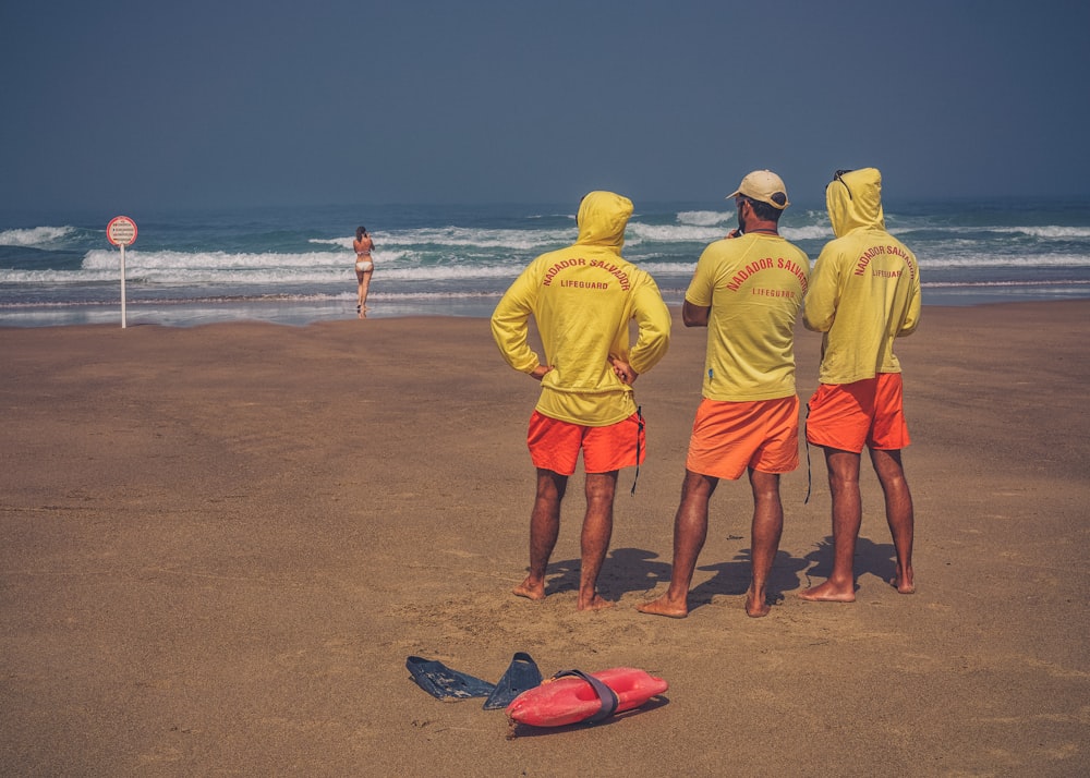 tres hombres de pie sobre la arena marrón protagonizando a una mujer de pie en la orilla del mar