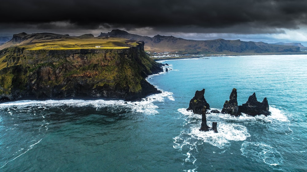 pilas de mar negro rodeadas por un cuerpo de agua al lado de la montaña bajo un cielo nublado