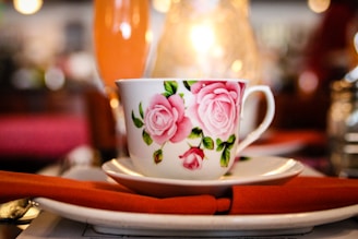 A vibrant pink tea cup surrounded by fresh rose petals and delicate gold accents.