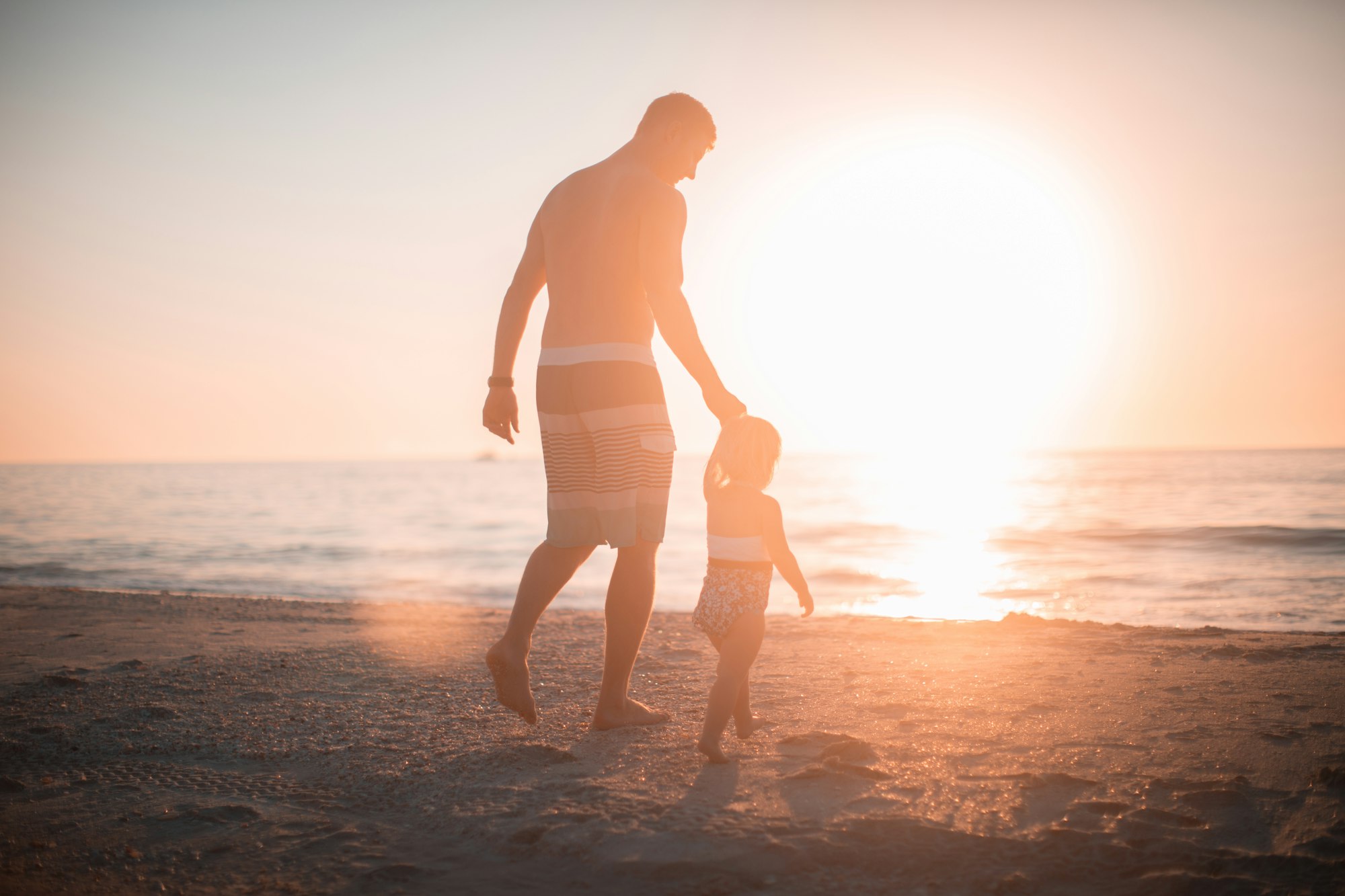 Father and daughter walking on a beach with sunset