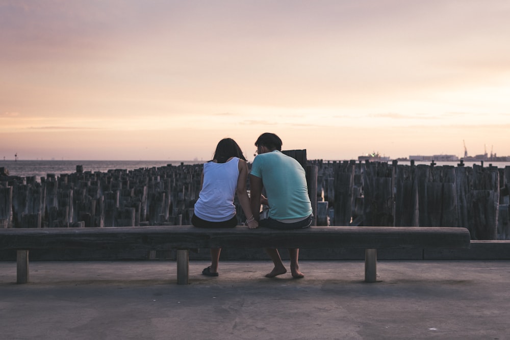 man and woman sitting on bench facing on body of water