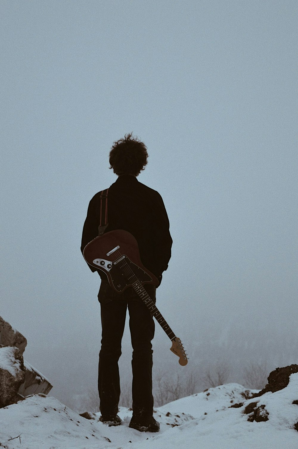 homme avec guitare sur son dos debout sur la falaise