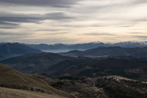 A panoramic view from a mountain summit overlooking layered ridges and distant villages