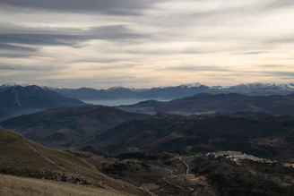A panoramic view from a mountain summit overlooking layered ridges and distant villages