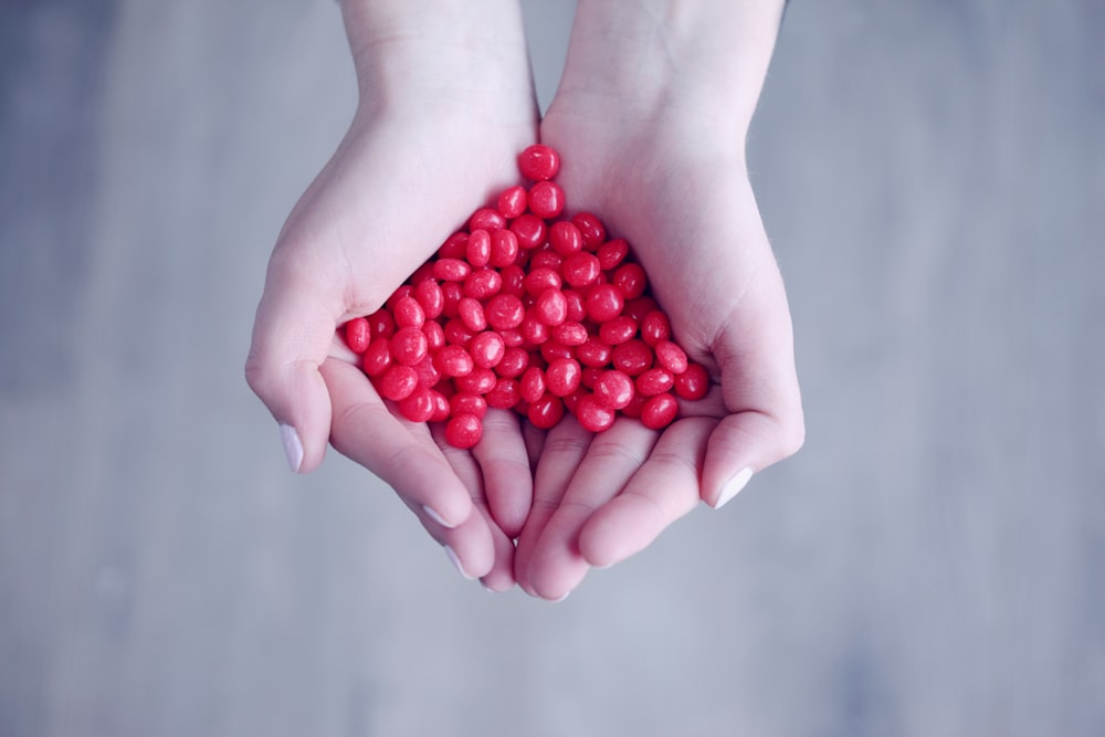 pessoa segurando doces vermelhos nas palmas das mãos