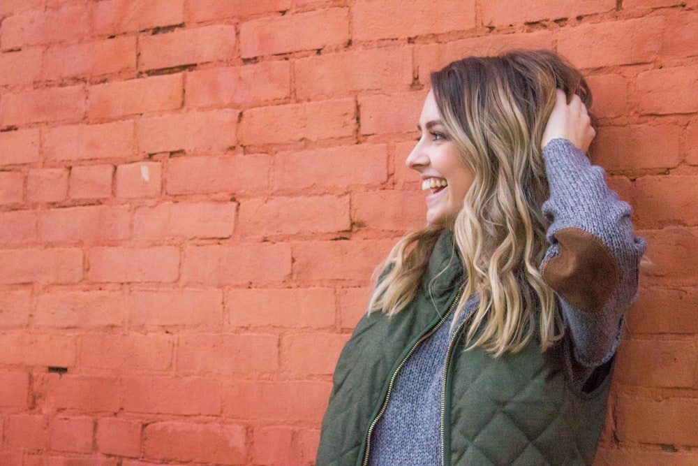 woman holding her her while leaning on red brick wall