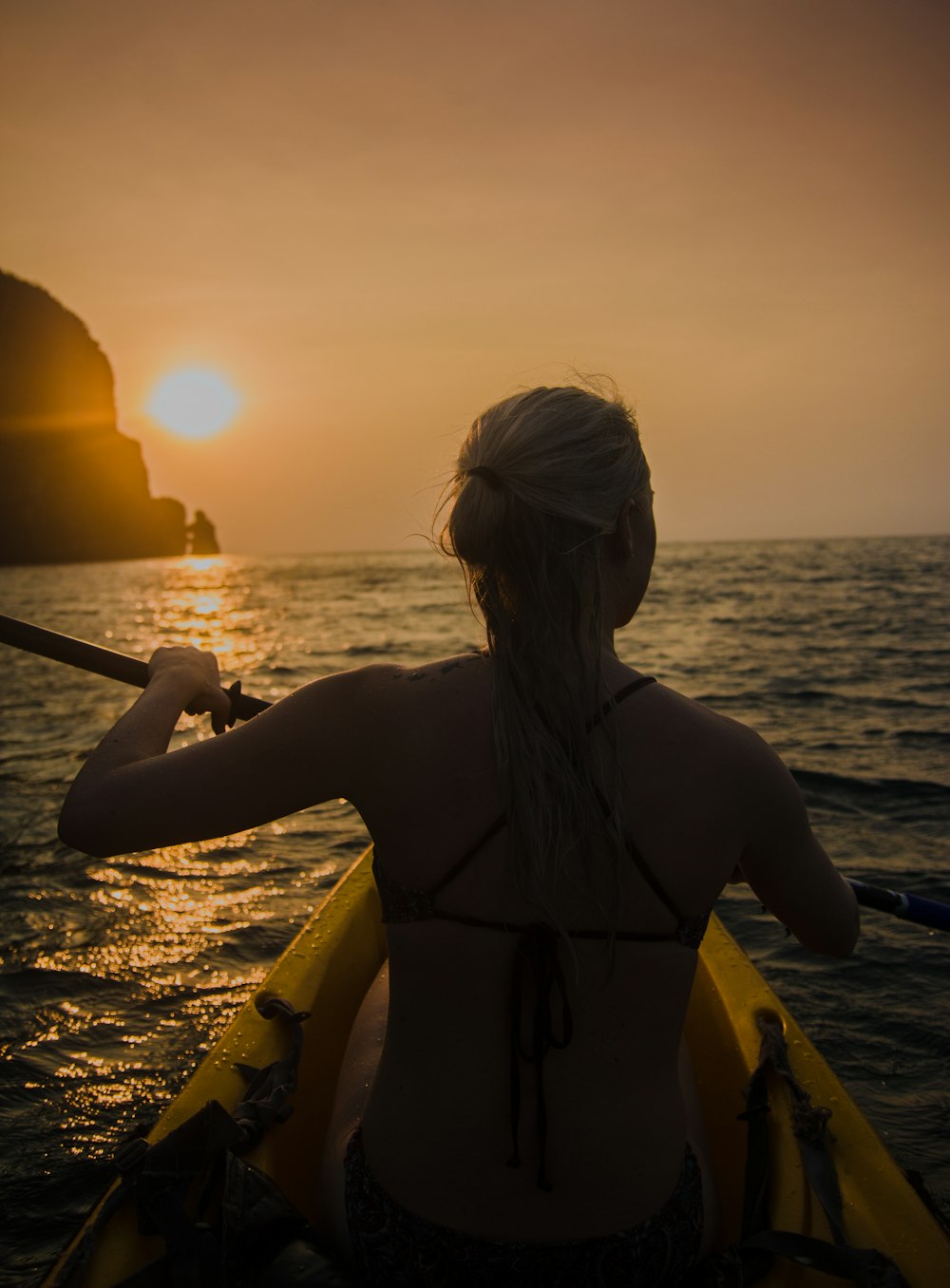 woman kayaking facing sunset