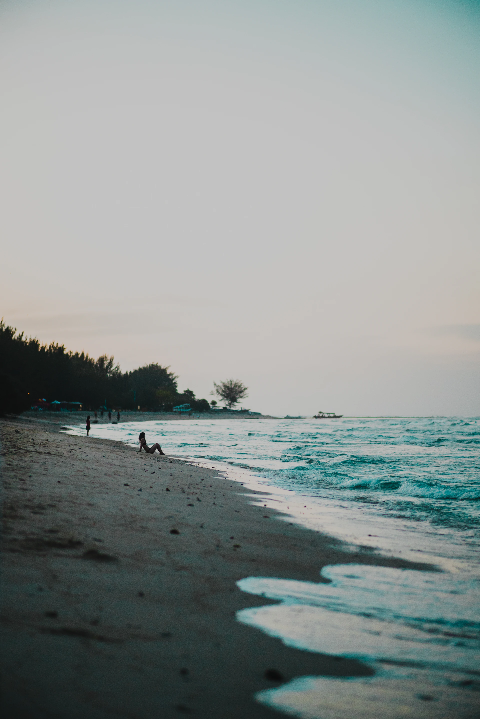 A peaceful beach scene at dusk with gentle waves lapping against the shore and a silhouette of a lone traveler gazing at the horizon.