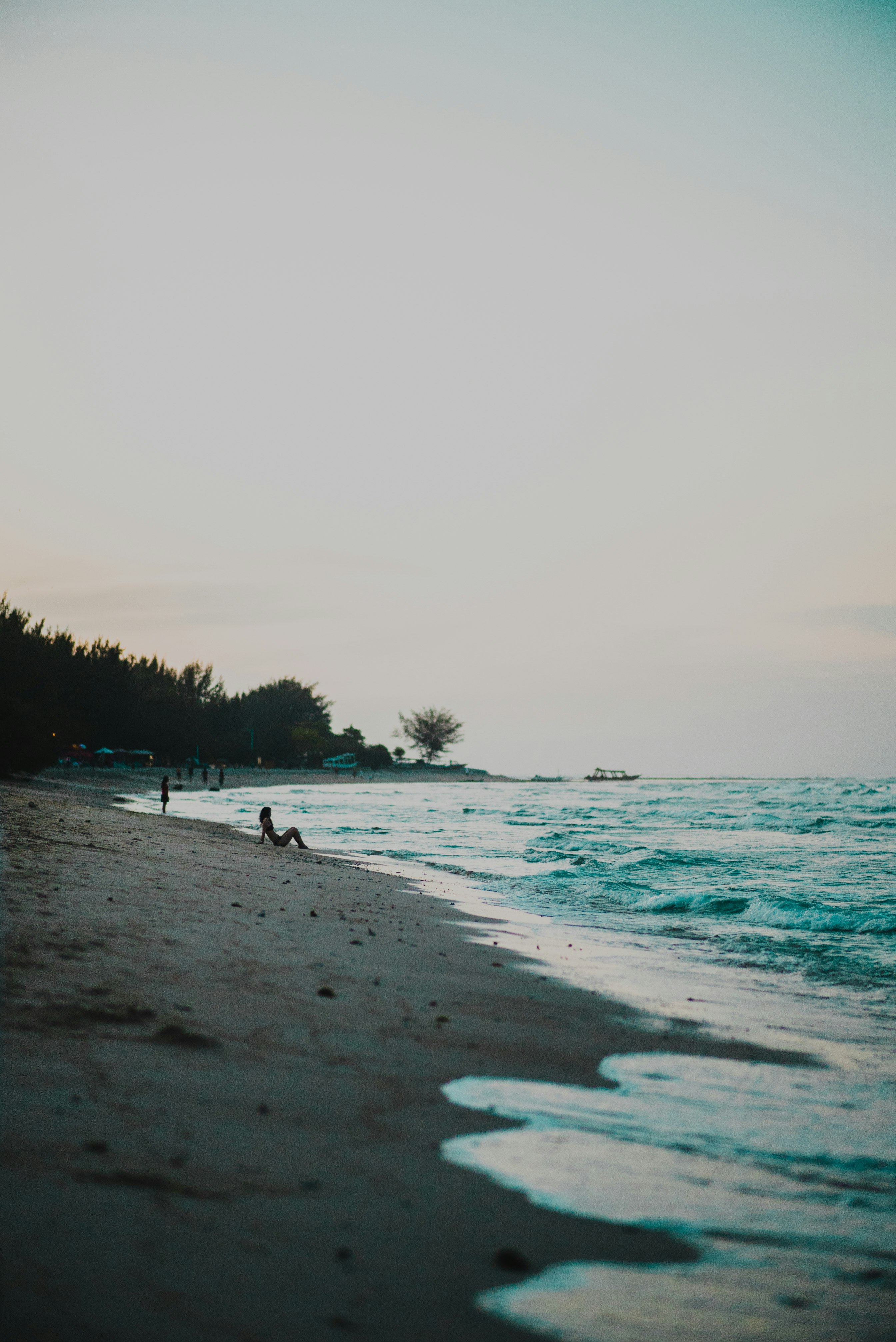 person sitting on shore looking at waves