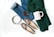 A neatly arranged flat lay featuring a pair of jeans, a green knitted sweater, a pair of patterned loafers, a metal belt, a mug labeled 'COFFEE', and a bowl of coffee beans. The items are placed on a white background, indicating a casual, cozy theme.
