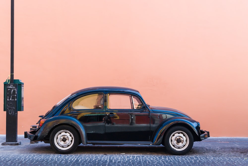 black Volkswagen Beetle beside beige wall