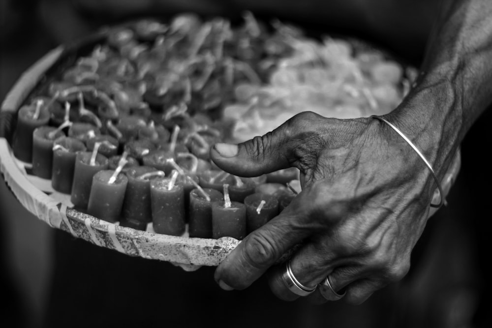 grayscale photography of person holding tray with candle lot