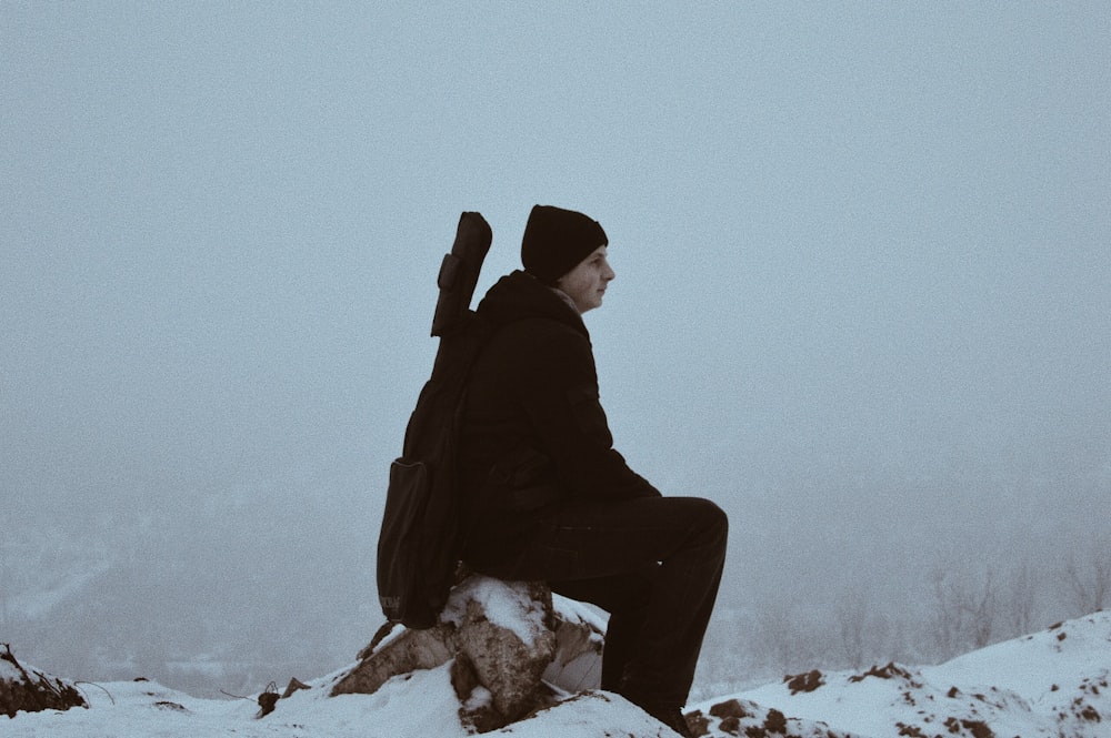 man sitting on brown stone surrounded by snow