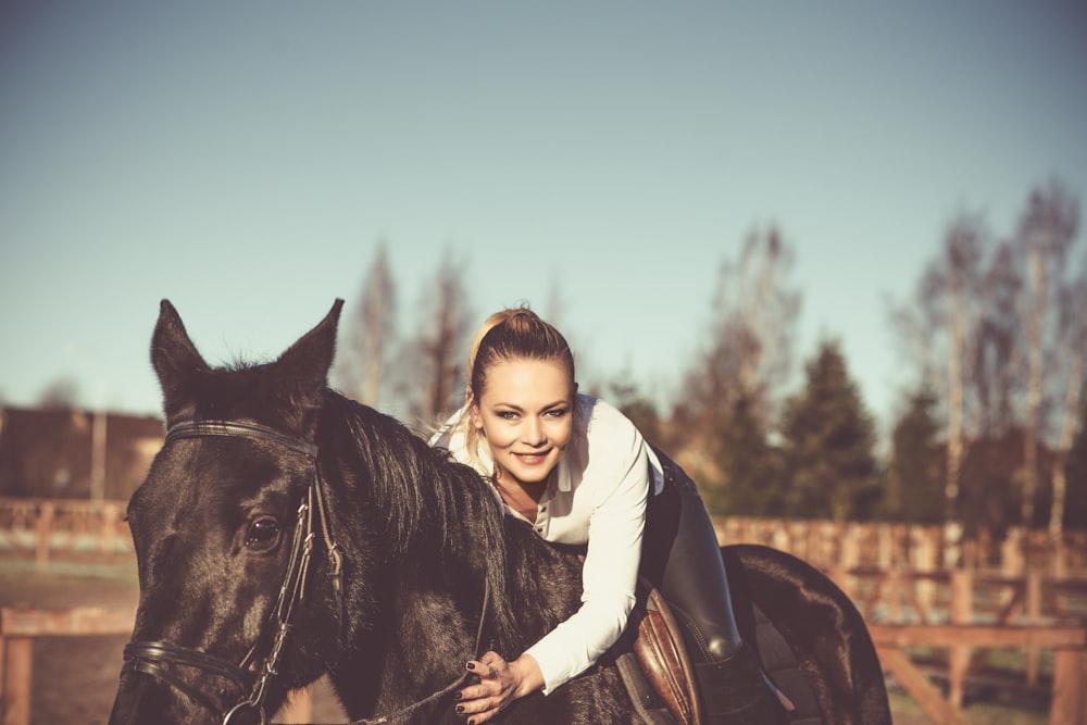 femme en sweat à capuche blanc chevauchant un cheval noir