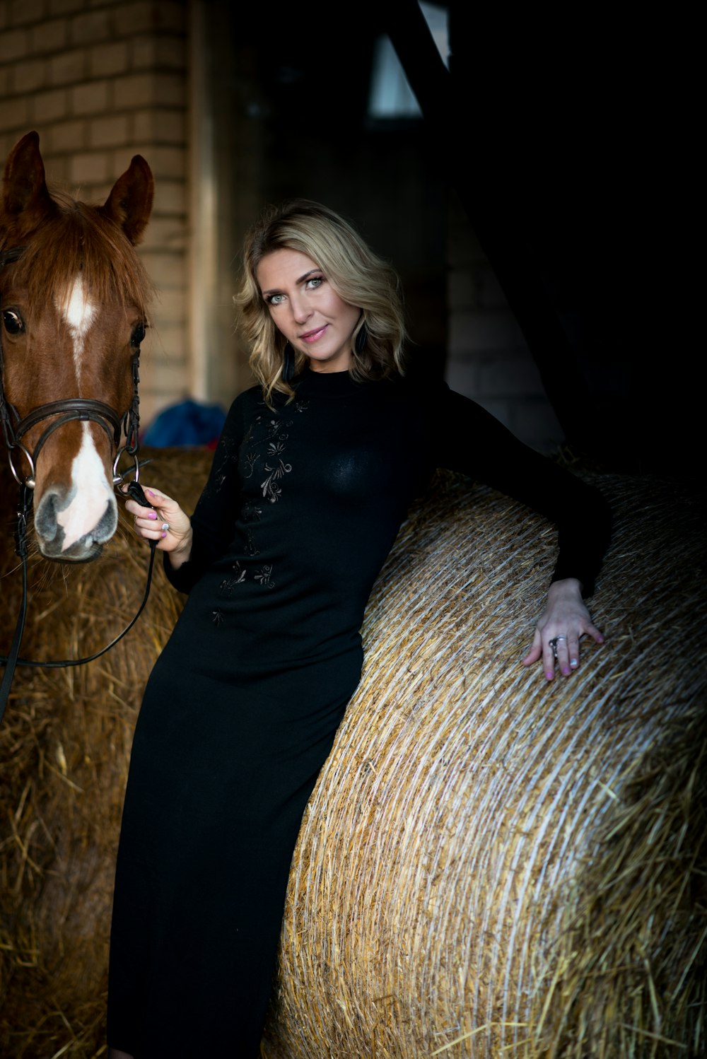 woman holding the horse strap while leaning on hay