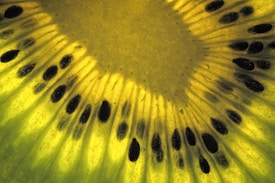 A close-up view of a kiwi slice, showing the intricate patterns of its seeds arranged in a circular formation. The details of the fruit's texture and vibrant yellow-green color are clearly visible.