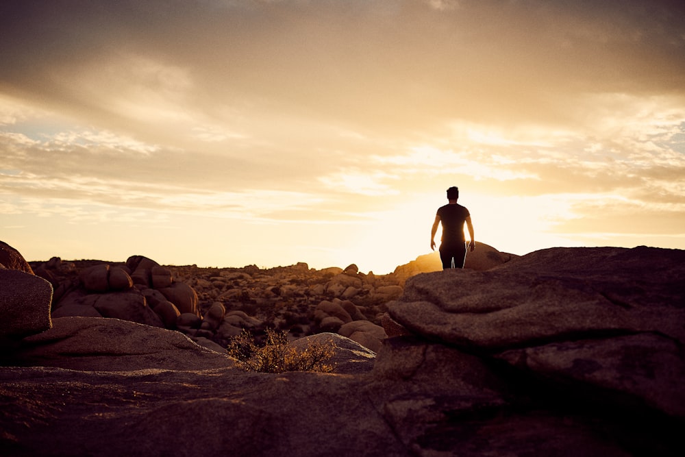 man walking on gray rocks under yellow sky during daytime