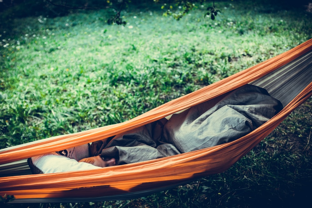 person lying on orange hammock outdoors