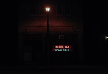 A dimly lit street scene at night features a brick building with a neon sign displaying the words 'INCOME TAX' in red and 'NOTARY PUBLIC' in green. A streetlight illuminates the space immediately around it, creating a contrast with the dark surroundings.