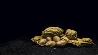 A pile of unshelled peanuts and shelled peanuts sits on a dark textured surface. The shells are rough and earthy, while the peanuts are smooth and light brown in color.