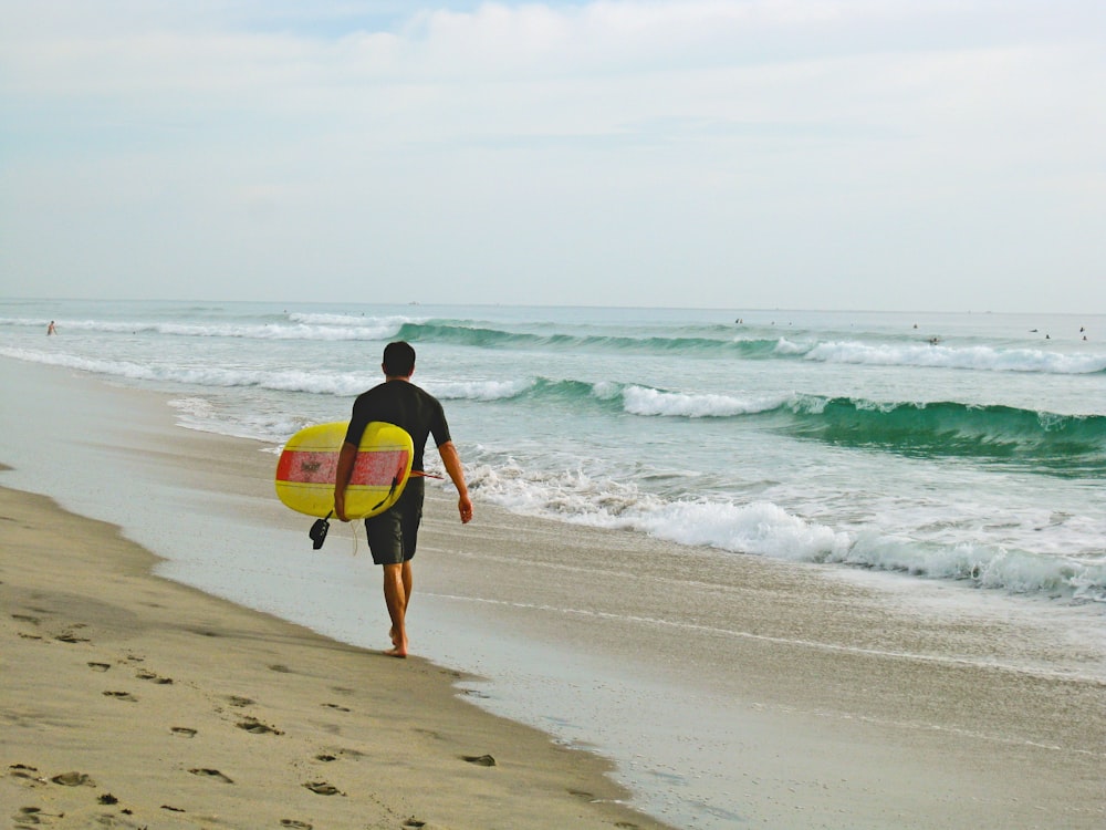 Hombre que lleva una tabla de surf mientras camina por la orilla