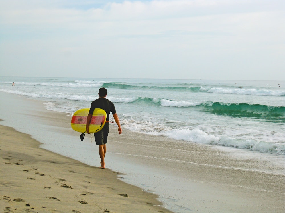 homem carregando prancha de surf enquanto caminha na costa