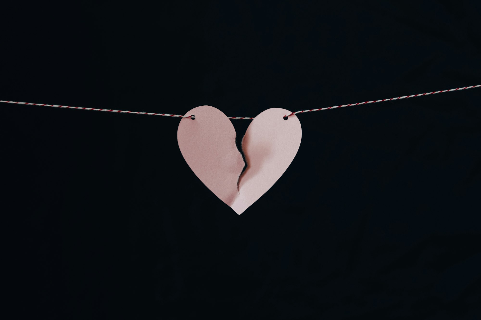 a torn pink paper heart hanging from a string against a black background