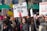 A large group of people participating in a protest or rally, holding various signs with messages related to social or political causes. The central sign reads 'Vote me for President 2050' with a red arrow pointing downward. Many participants are wearing winter clothing, indicating a cold weather setting.