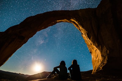 two person sitting under rock monolith wonder zoom background