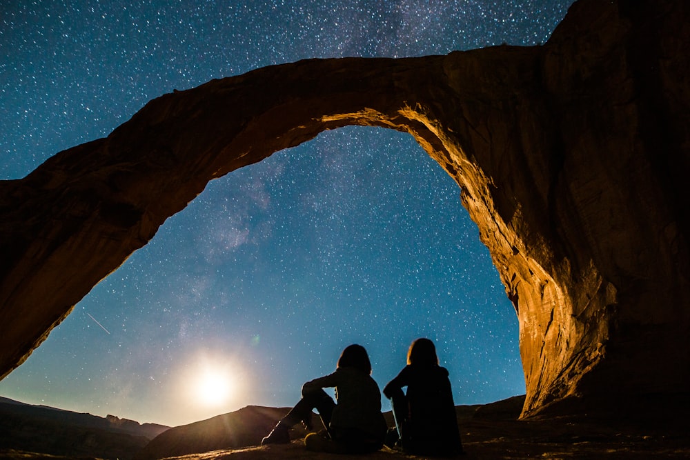 two person sitting under rock monolith