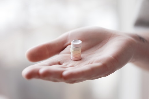 A hand is holding a small stack of pastel-colored cylindrical tablets. The background is softly blurred, with a calm and neutral tone.