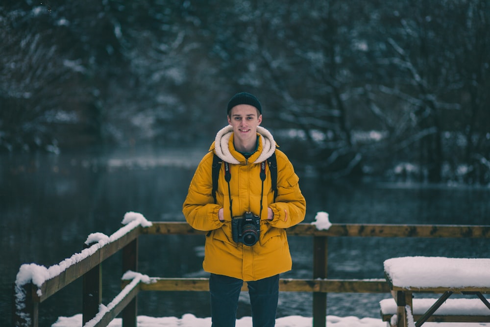 man standing next to brown fence beside body of water