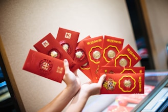 A hand holds several red envelopes with gold designs and coins inserted. The envelopes feature traditional Chinese symbols and characters.
