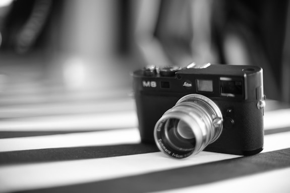 A vintage-style camera with a prominent lens is placed on a surface with black and white stripes. The camera has a textured body and a classic design, evoking a sense of nostalgia.