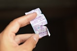 A hand holding torn pieces of a ticket with numbers and Thai writing on it. The background is blurred and dark, making the pieces in the foreground stand out.