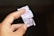 A hand holding torn pieces of a ticket with numbers and Thai writing on it. The background is blurred and dark, making the pieces in the foreground stand out.