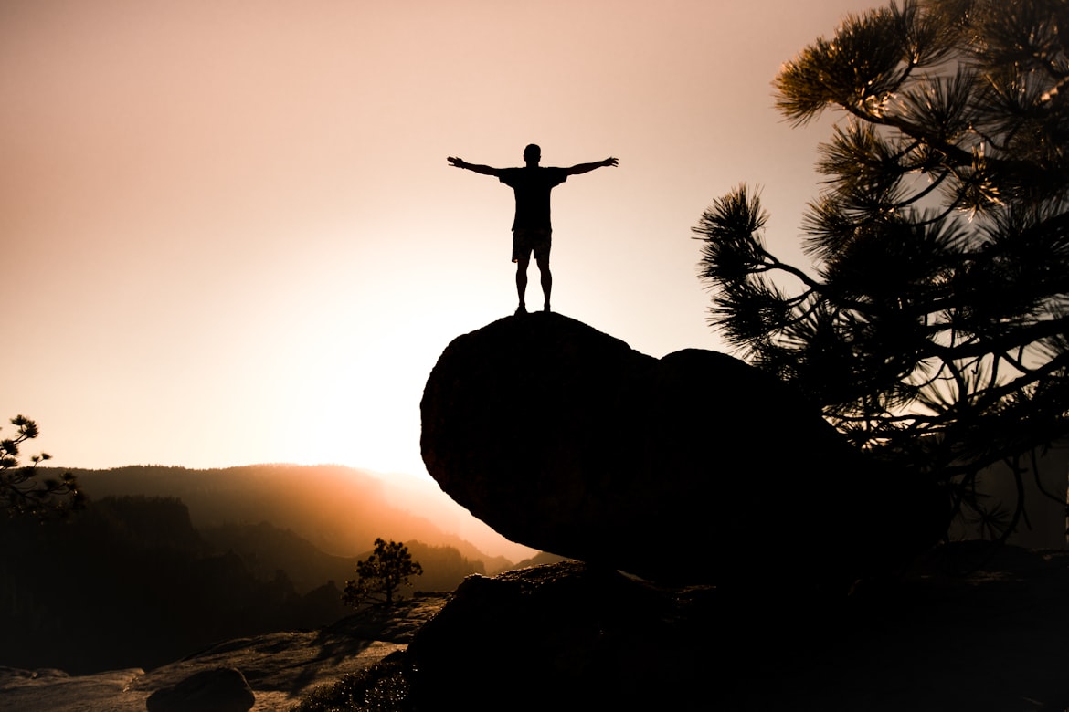 man standing on a cliff and with outstretched arms facing the sun