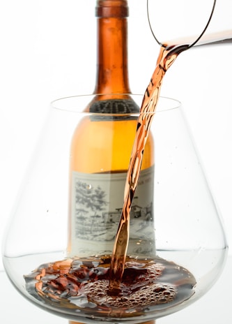 Close-up of a hand pouring amber spirit into a glass, with soft waves reflected in the liquid.