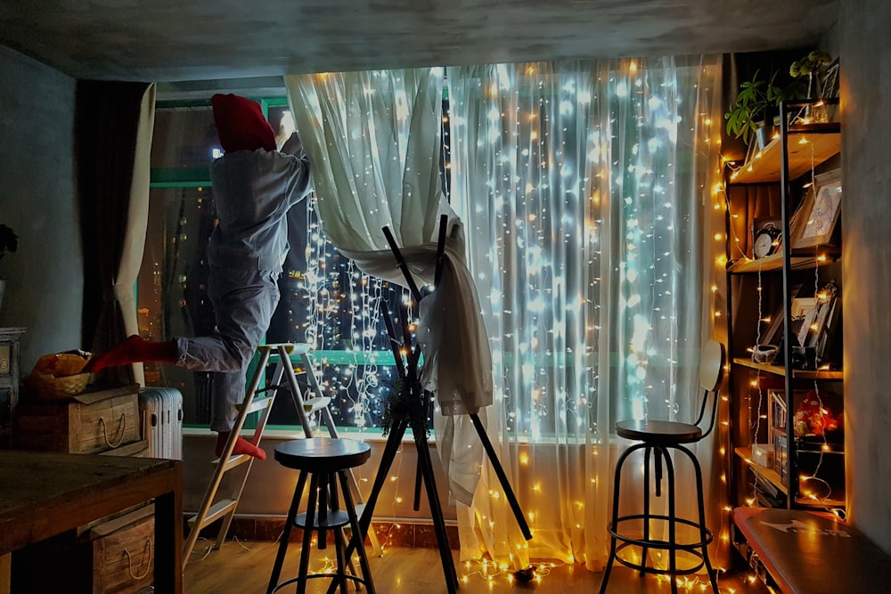 person standing on step ladder in front of string lights