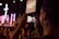 A person is holding a smartphone to capture a live event, focusing on a stage with performers. The stage is illuminated with purple and pink lights, and a large cross is visible in the background. The scene appears to be in a dimly lit auditorium or venue filled with attendees.