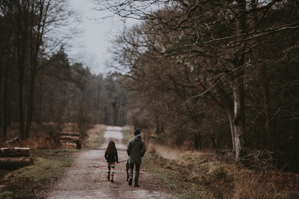 man and child walking on road surrounded by trees