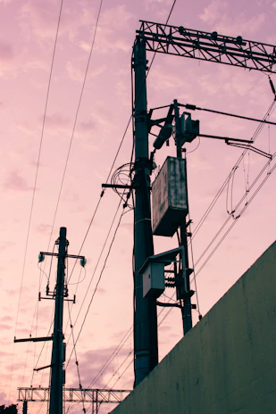 A close-up of a certified lineman using high-voltage hot sticks against a backdrop of power lines at dusk.