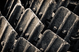 Rows of rugged, textured metallic plates with a dark, weathered appearance, arranged in a close-up pattern.