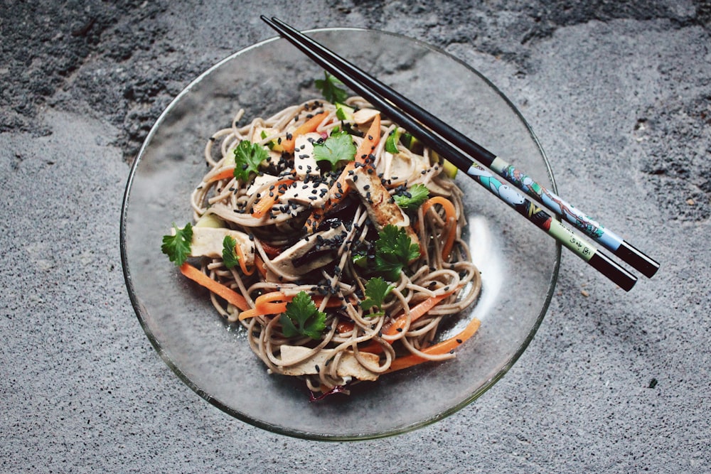 Fideos de verduras con palillo sobre plato de cristal