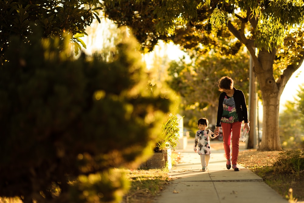 woman holding a child walking in the pathway